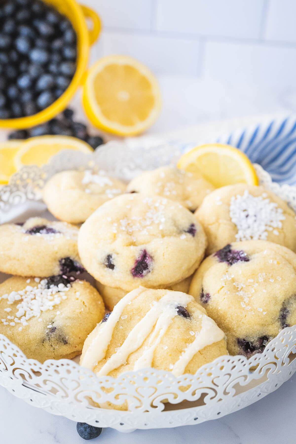 Lemon blueberry cookies on tray with fresh lemon and blueberries behind. 
