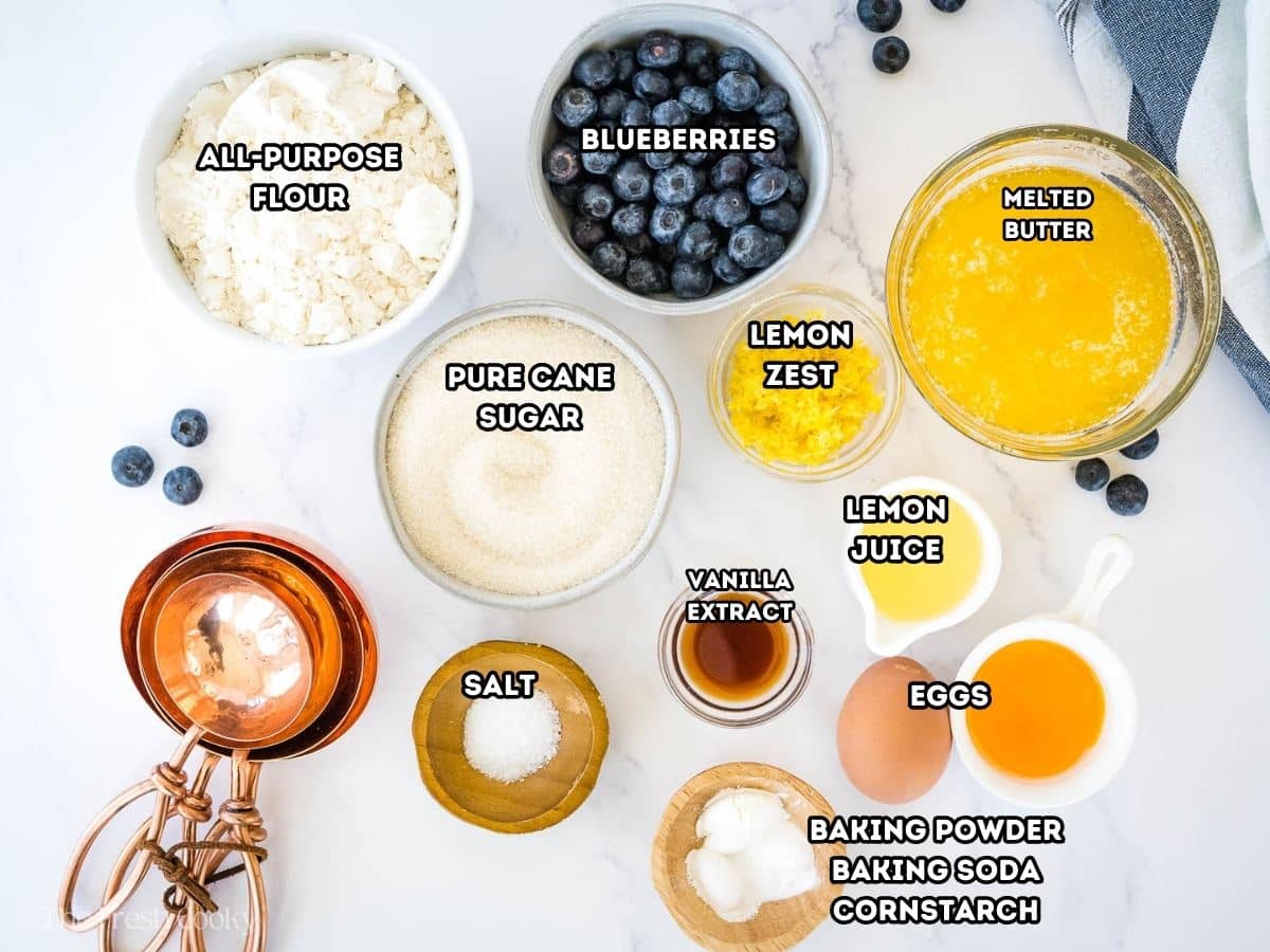 Labeled ingredients for lemon blueberry cookies, L-R - flour, blueberries, melted butter, lemon zest, lemon juice, eggs, vanilla extract, baking powder, soda, cornstarch, salt, pure cane sugar.