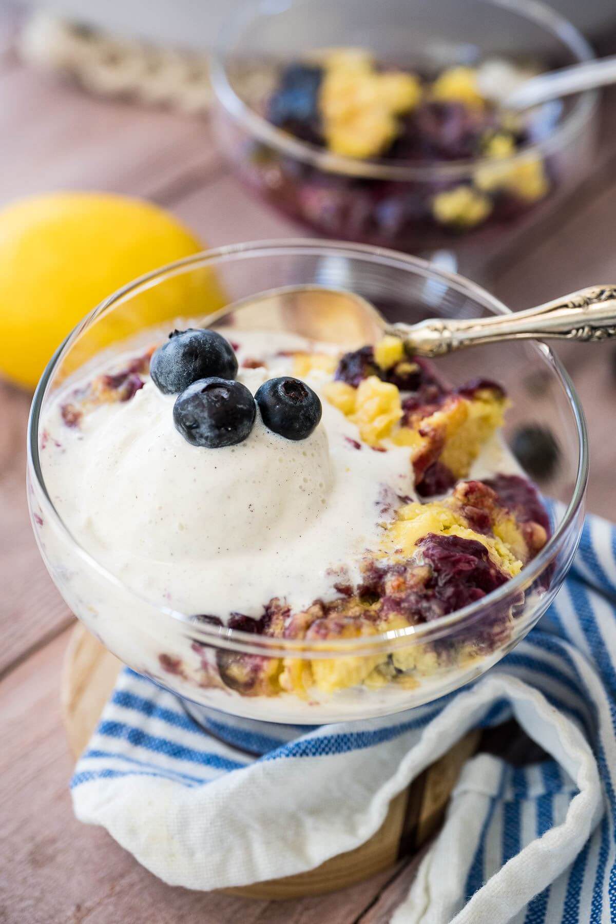 Spoons sit in two serving bowls full of cake, blueberries, and ice cream.