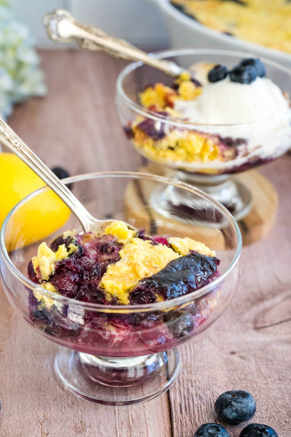 Two serving bowls are filled with yellow cake with blueberries, and one has ice cream on top.