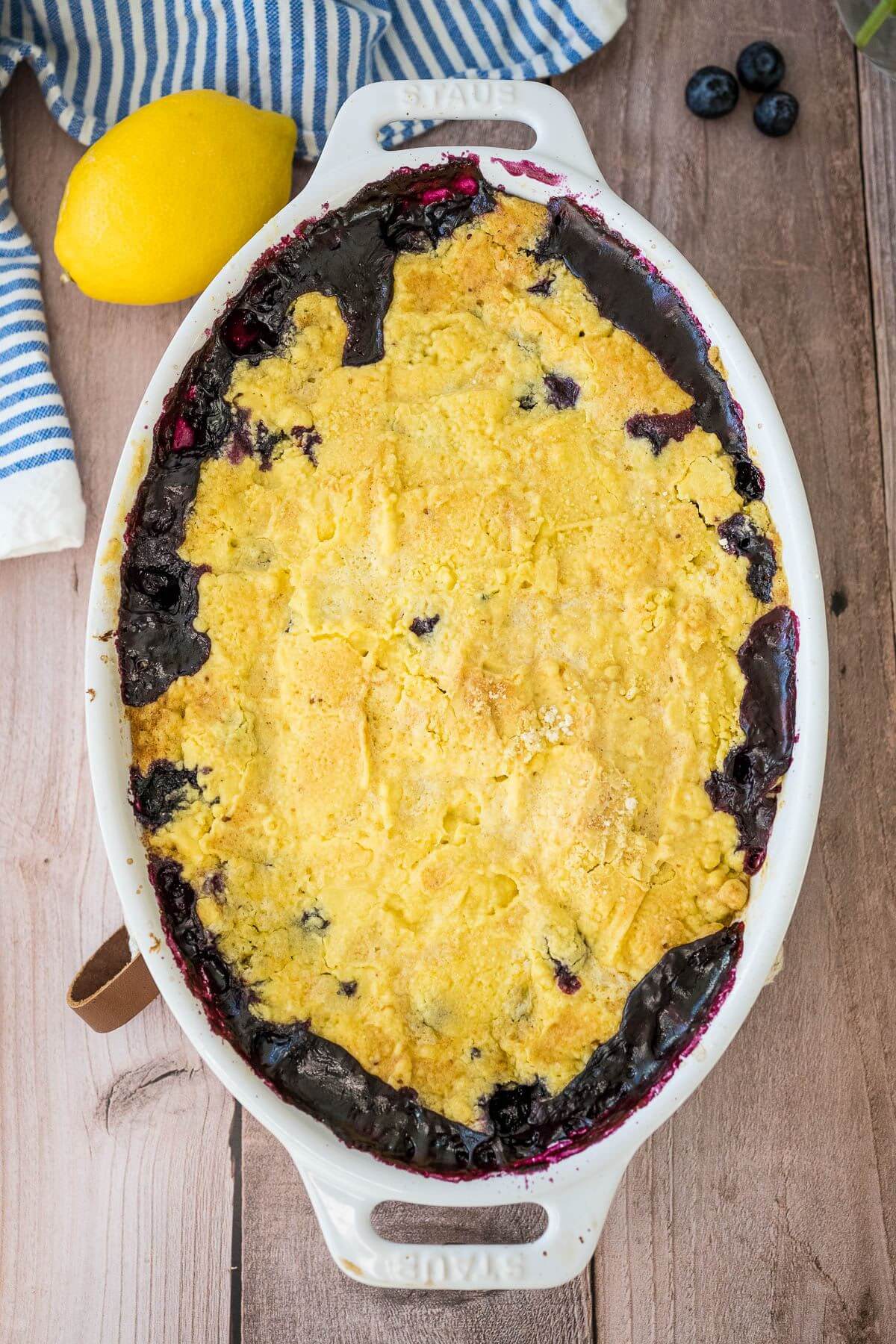 A full baking dish has a baked cake layer over purple cooked blueberries.
