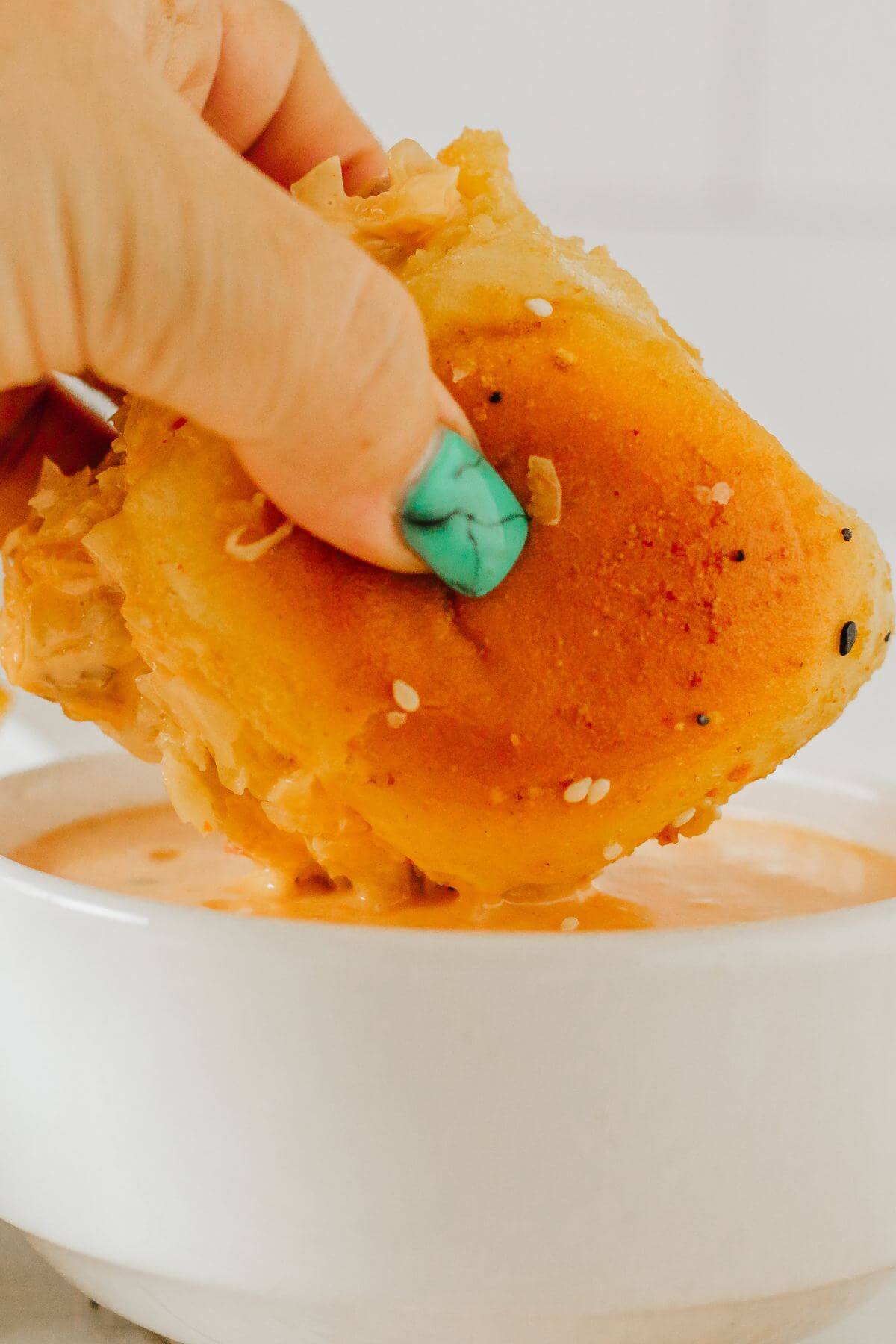 A hand dips a slider into a bowl of Thousand Island dressing.