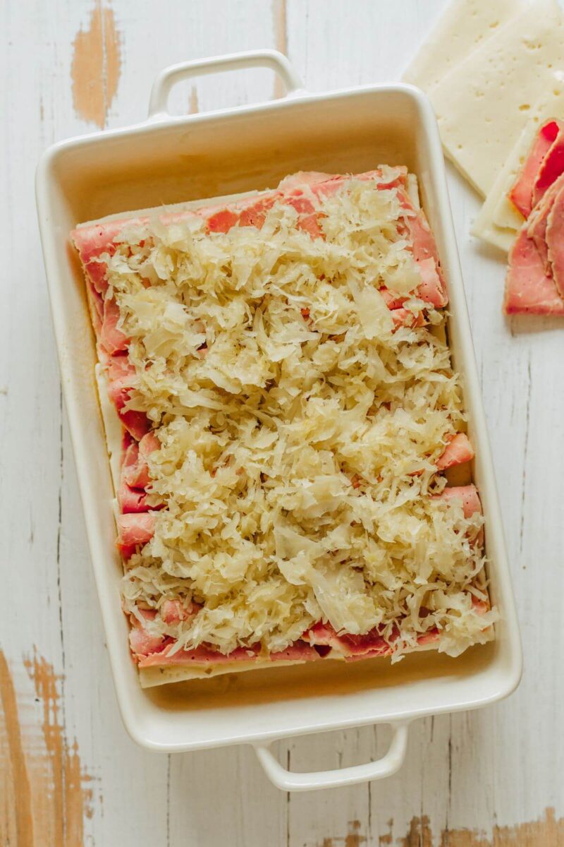 A whole pan is shown with saurkraut covering meaty sandwich layer.