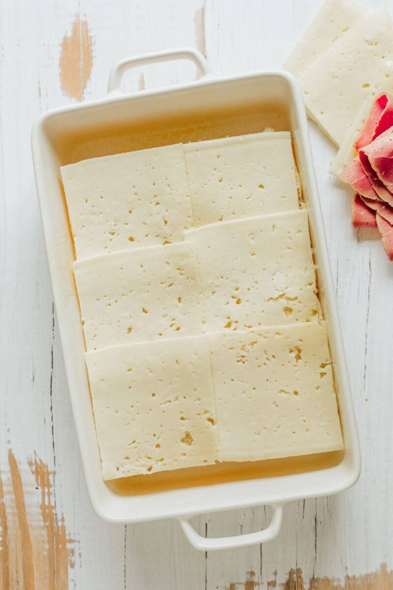 A whole baking dish is shown with slices of Swiss cheese layered.