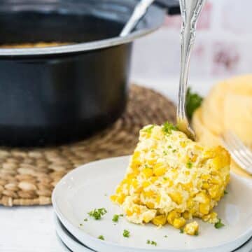 Serving of corn casserole without jiffy made in a crockpot, with crockpot behind.