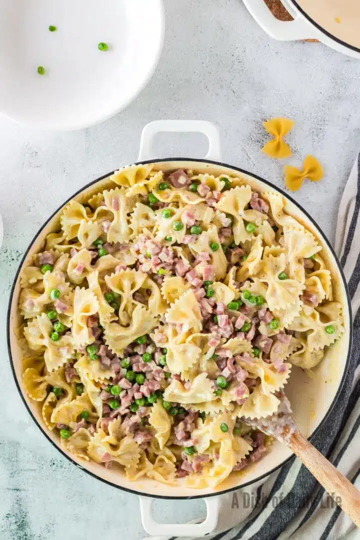 Ham and peas pasta in a pretty skillet with a wooden spoon.