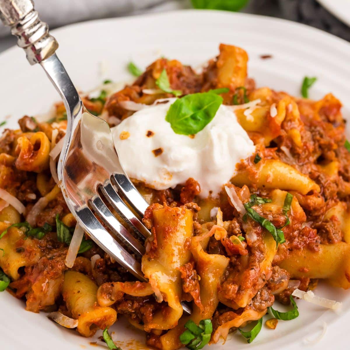 A serving of hamburger helper lasagna on a plate with a fork taking a bite. 