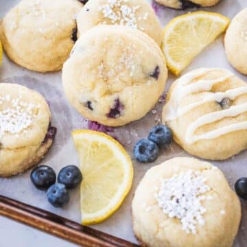Lemon blueberry cookies on baking sheet with slices of fresh lemon and fresh blueberries.