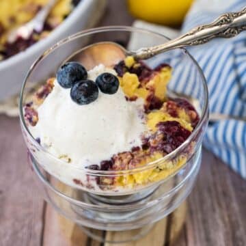 A serving of lemon blueberry dump cake in pretty dessert glasses served with a scoop of ice cream.