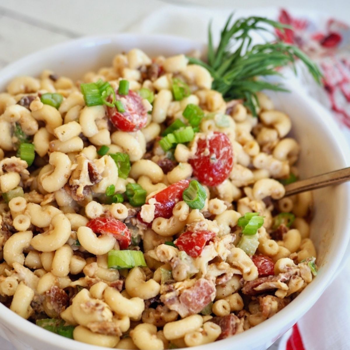 Bacon macaroni salad in a pretty white ceramic bowl garnished with fresh dill.