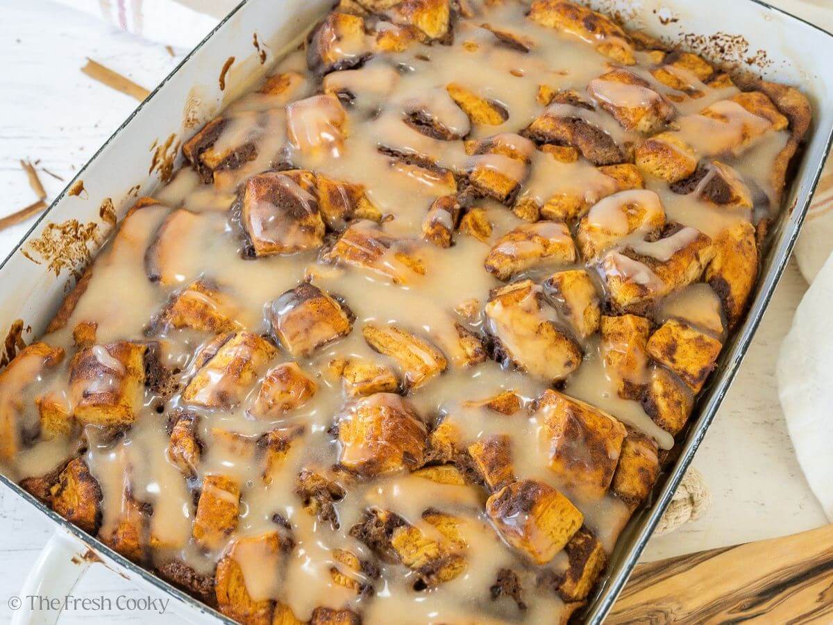 A gooey, glazed cinnamon roll casserole in a white pan.