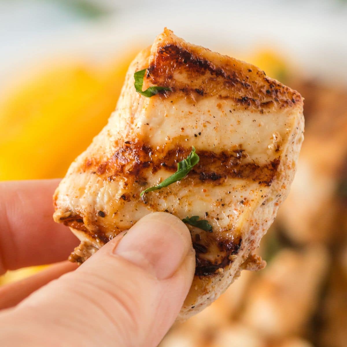 A hand holds up a juicy grilled chicken nugget.