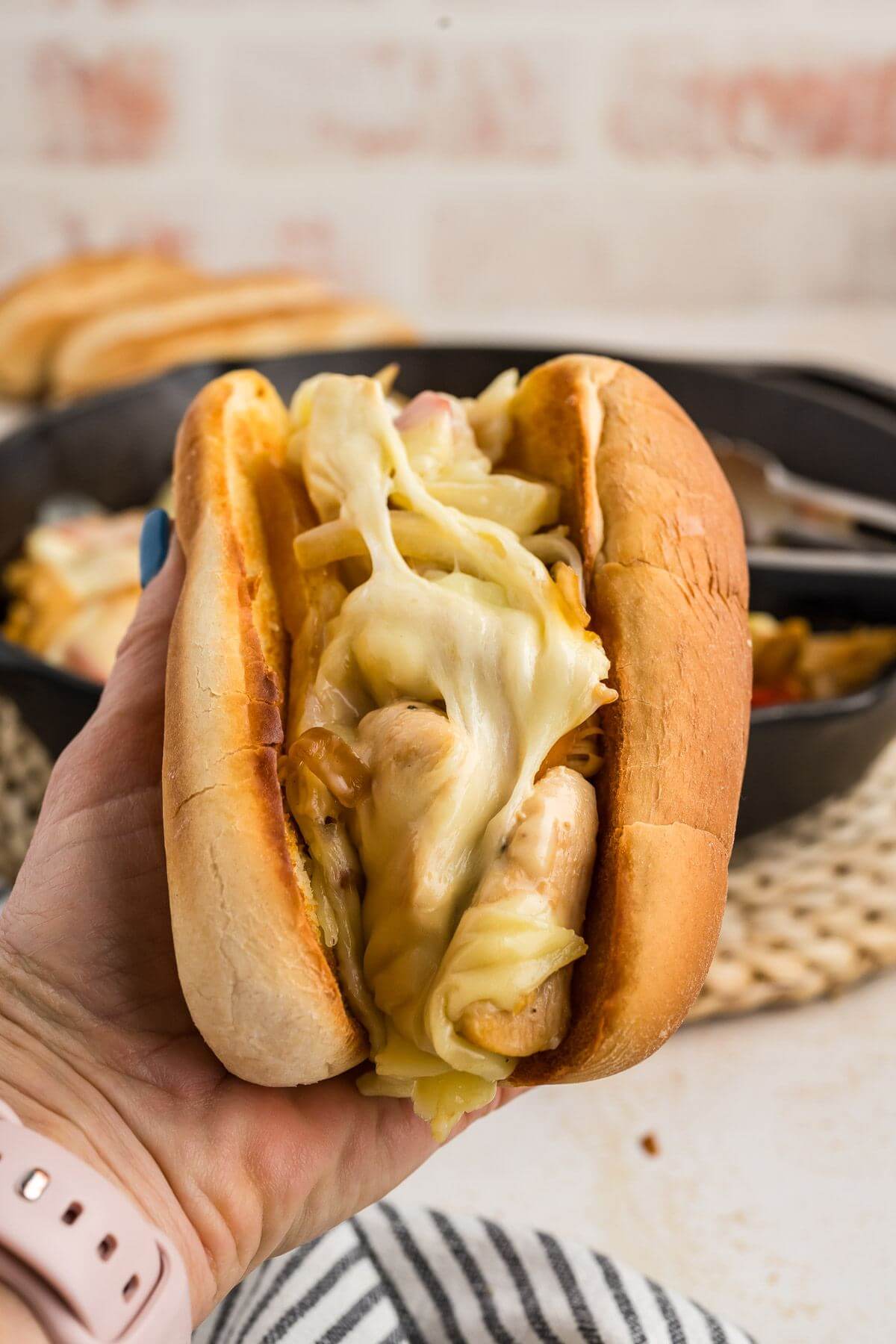 A hand holds up a thickly filled cheesesteak in a toasted Hoagie roll above a table.