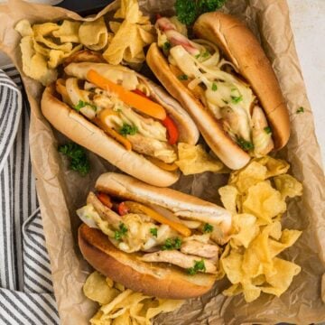 A tray filled with three chicken philly cheesesteaks with potato chips.