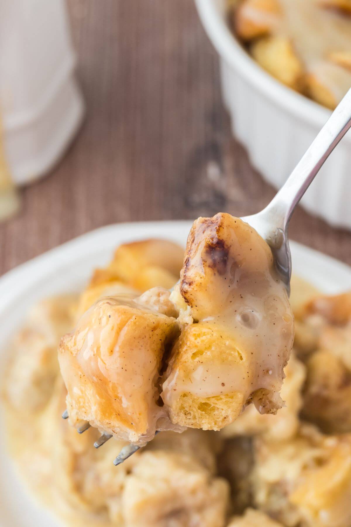 A fork lifts pieces of bread pudding up above the full baking dish of the same.