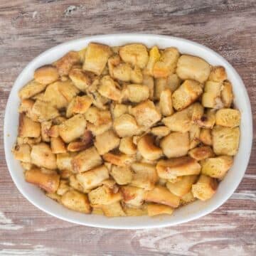 A large white baking dish is full of bread cubes baked golden brown and filled with custard that shows around edges.