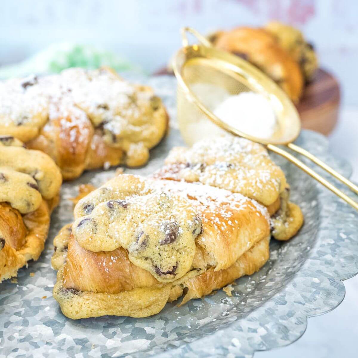 Le Crookies, cookie croissants on serving tray with powdered sugar sieve nearby.