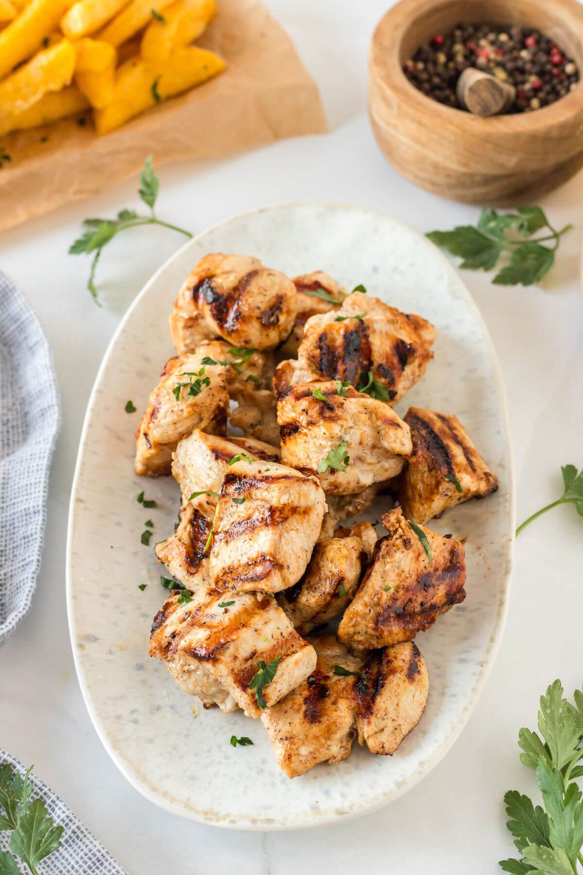 An oval plate is filled with grilled chicken chunks near black pepper and yellow pepper.