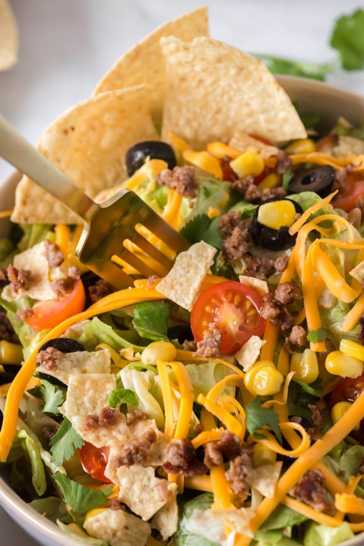 A fork dives into a full bowl of salad with cheese, tomatoes, lettuce, beef, and beans.