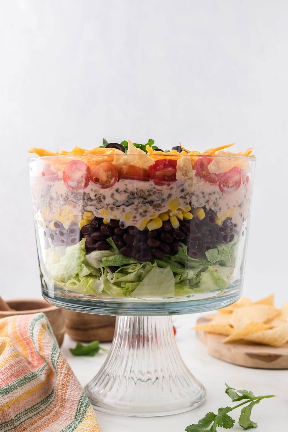 A side view of a filled glass dish shows salad with beans, corn, tomatoes, cheese, and beef.