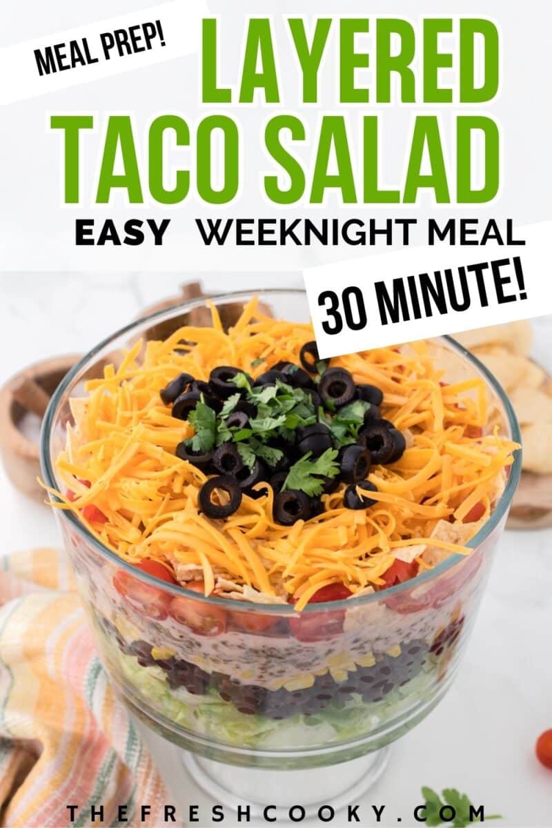A layered taco salad with lettuce, beans, taco meat, tomates, salsa dressing and topped with cheese, olives and cilantro to pin.