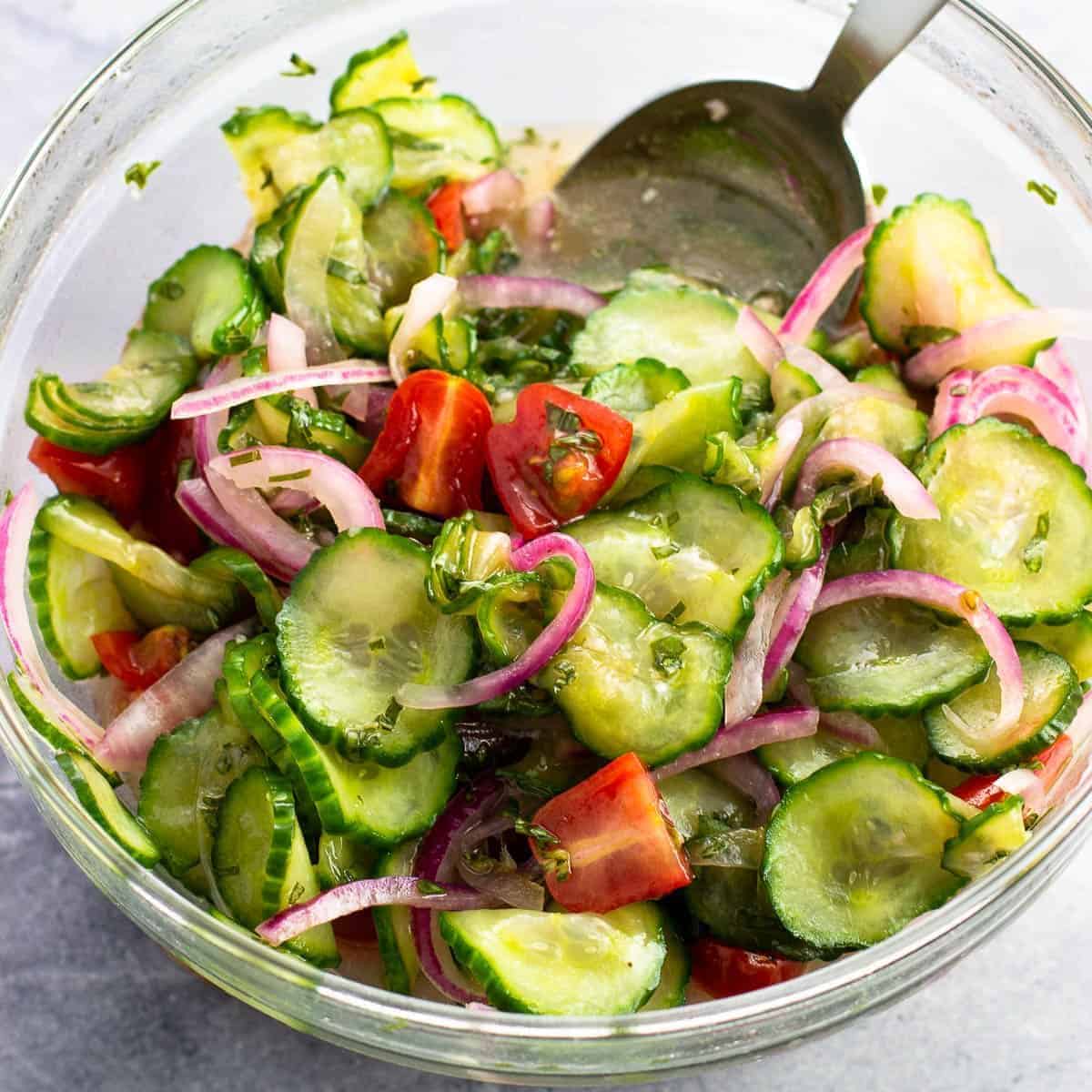 Marinated Cucumber Tomato Onion Salad in a glass bowl with a serving spoon.