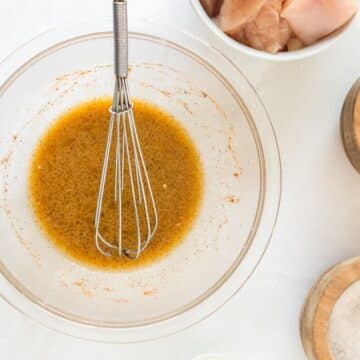 Marinade or brine ingredients in a glass bowl with raw chicken in background.