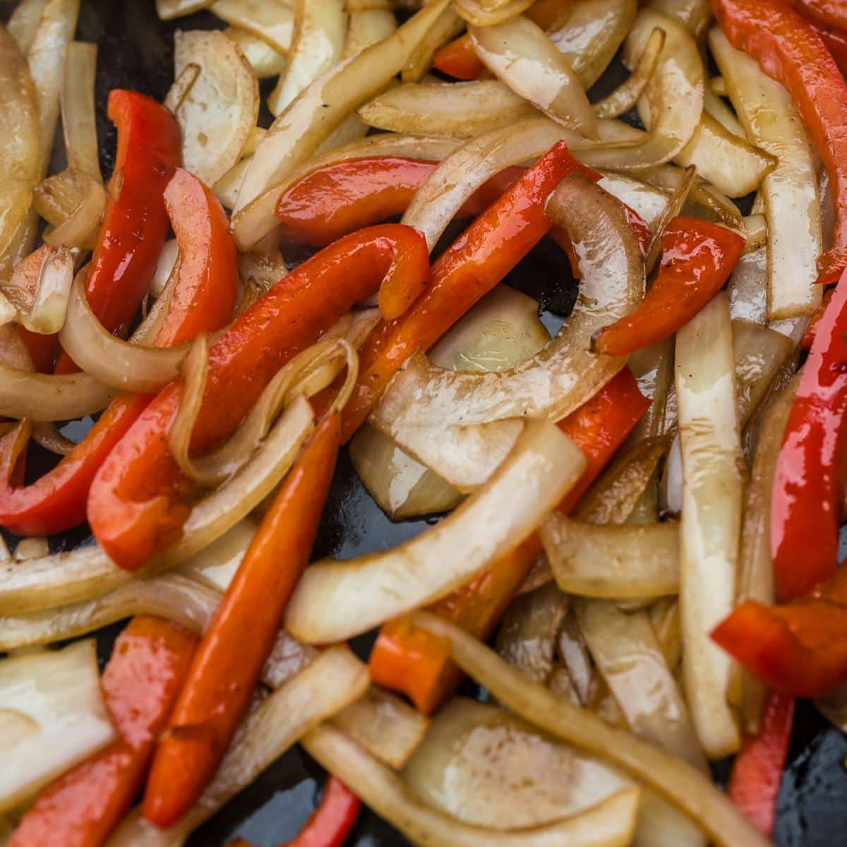 Orange and red bell pepper strips and onion cook on Blackstone.