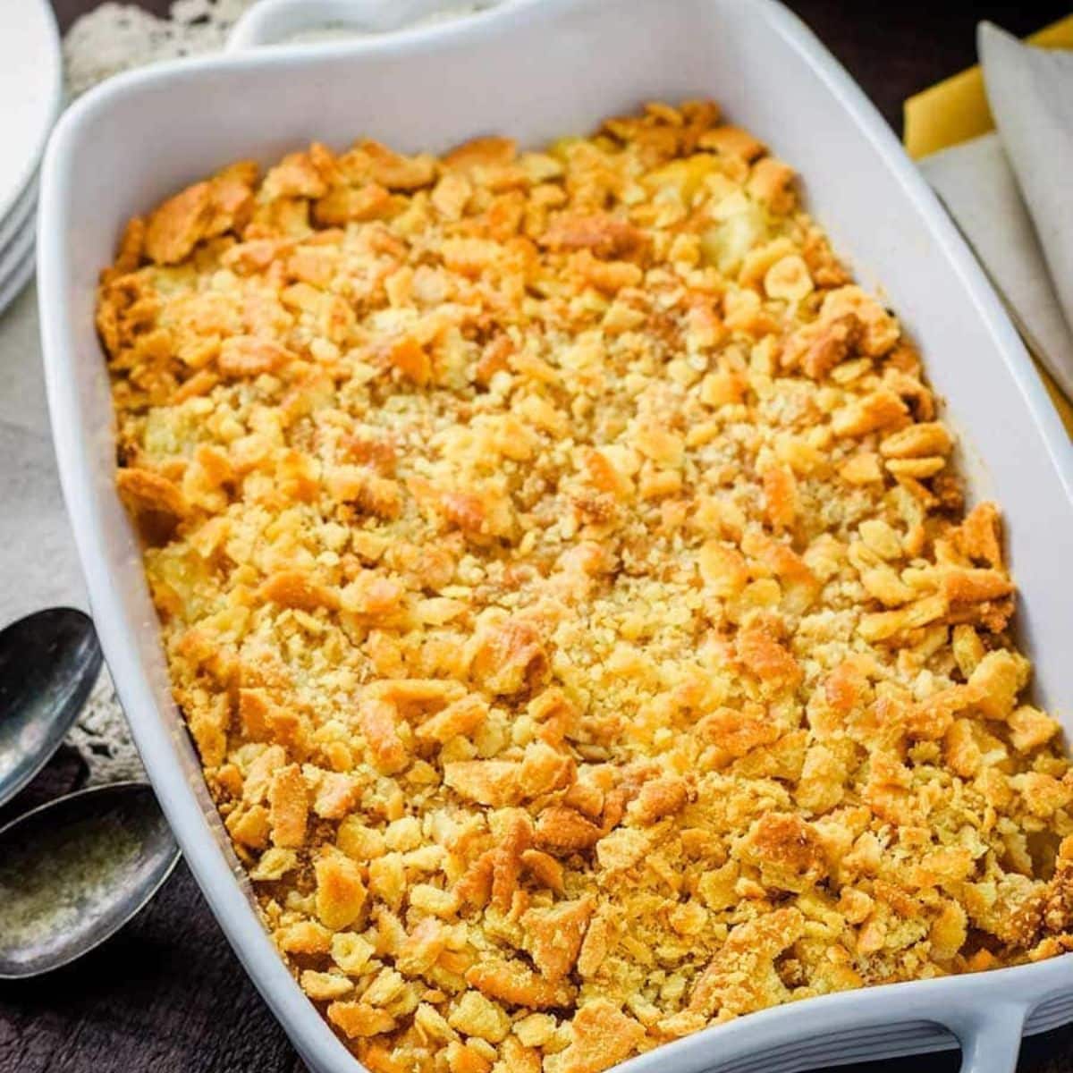 Pineapple Casserole in a casserole dish, with serving spoons.