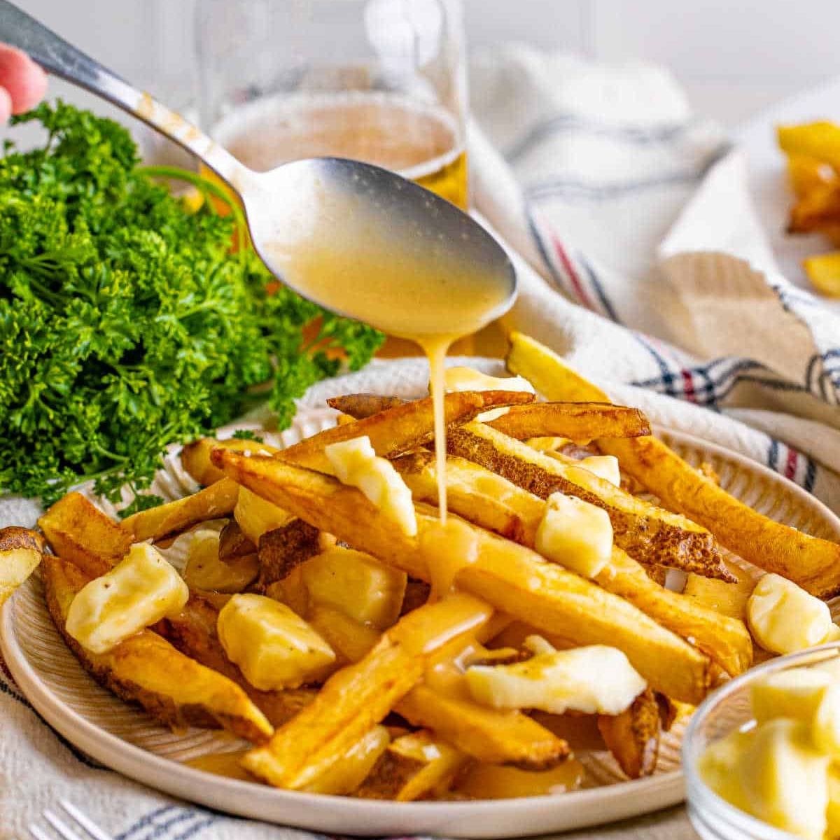 A plate filled with thick and crispy fries, drizzling with gravy for poutine fries.