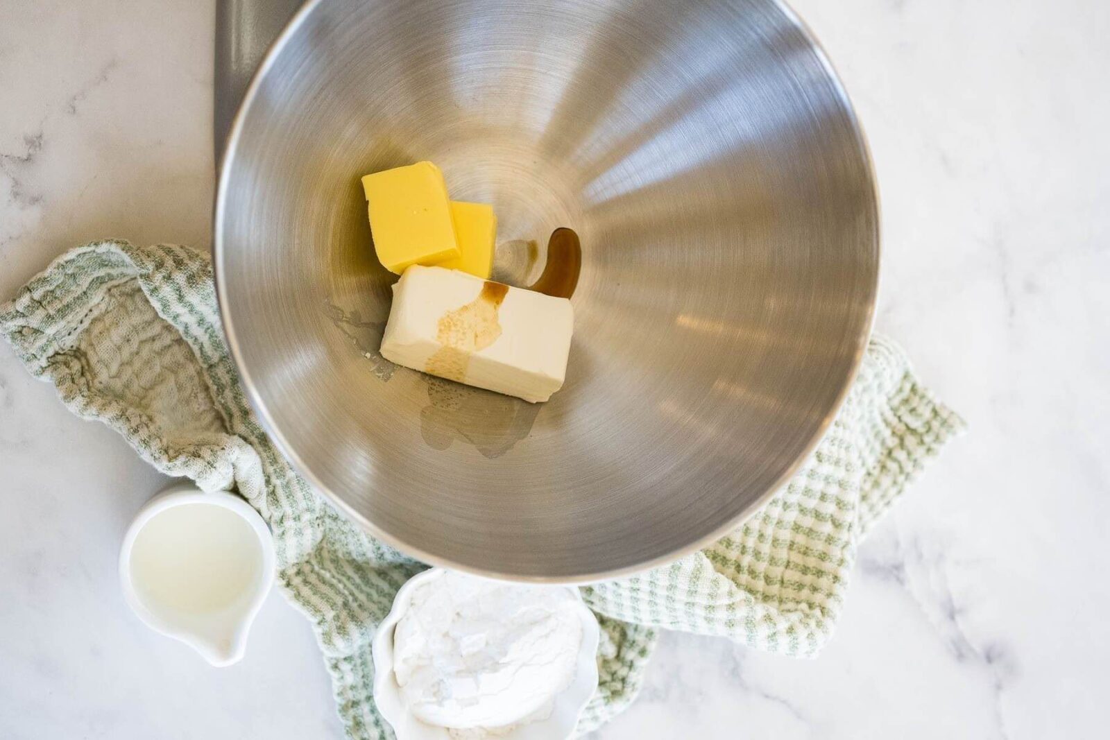 Squares of butter, a block of cream cheese, and vanilla sit in a metal bowl.