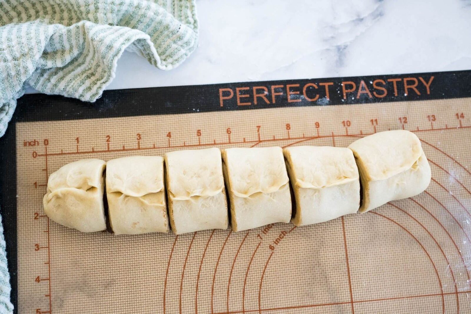 A rolled log of dough is sliced into 6 sections on a cutting board.