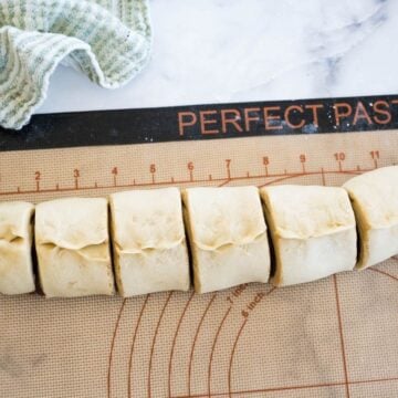 A rolled log of dough is sliced into 6 sections on a cutting board.