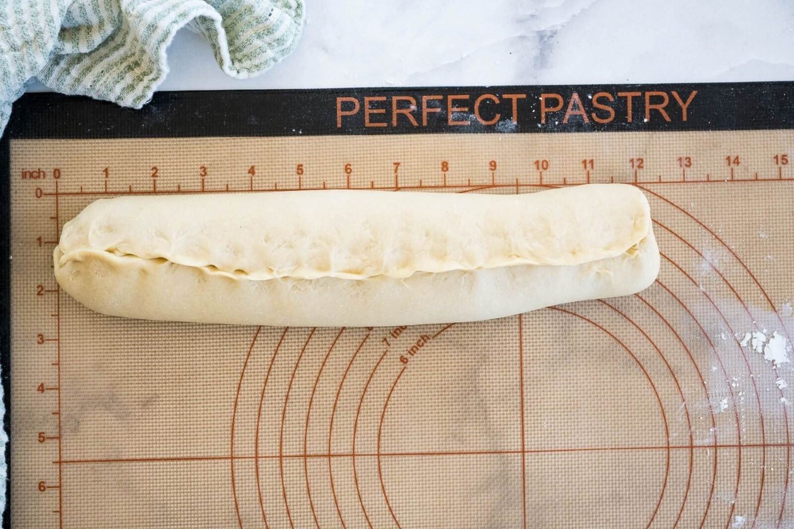 A rolled log of dough sits on a rolling board.