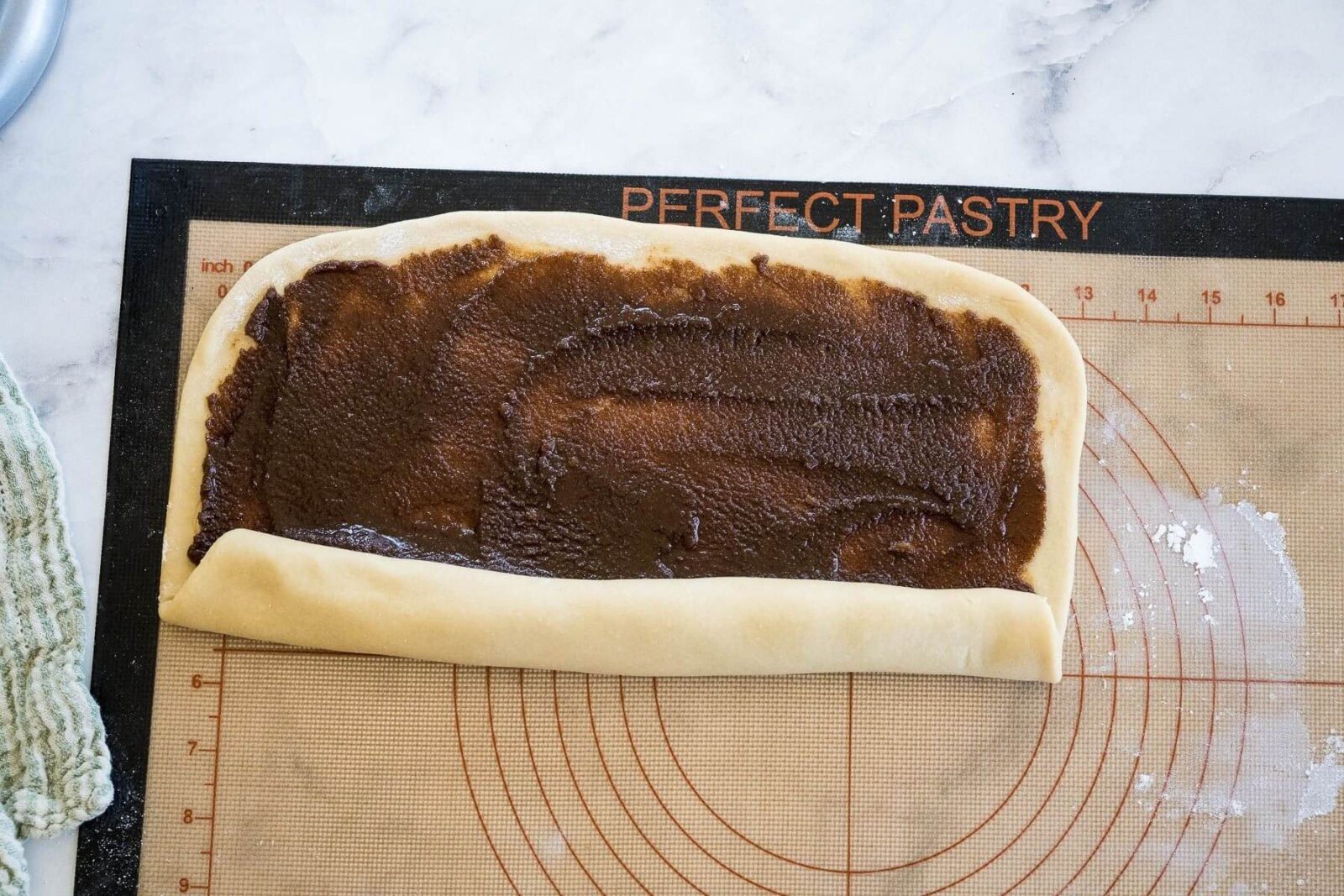 A slab of cinnamon covered dough has one long side starting to roll up.