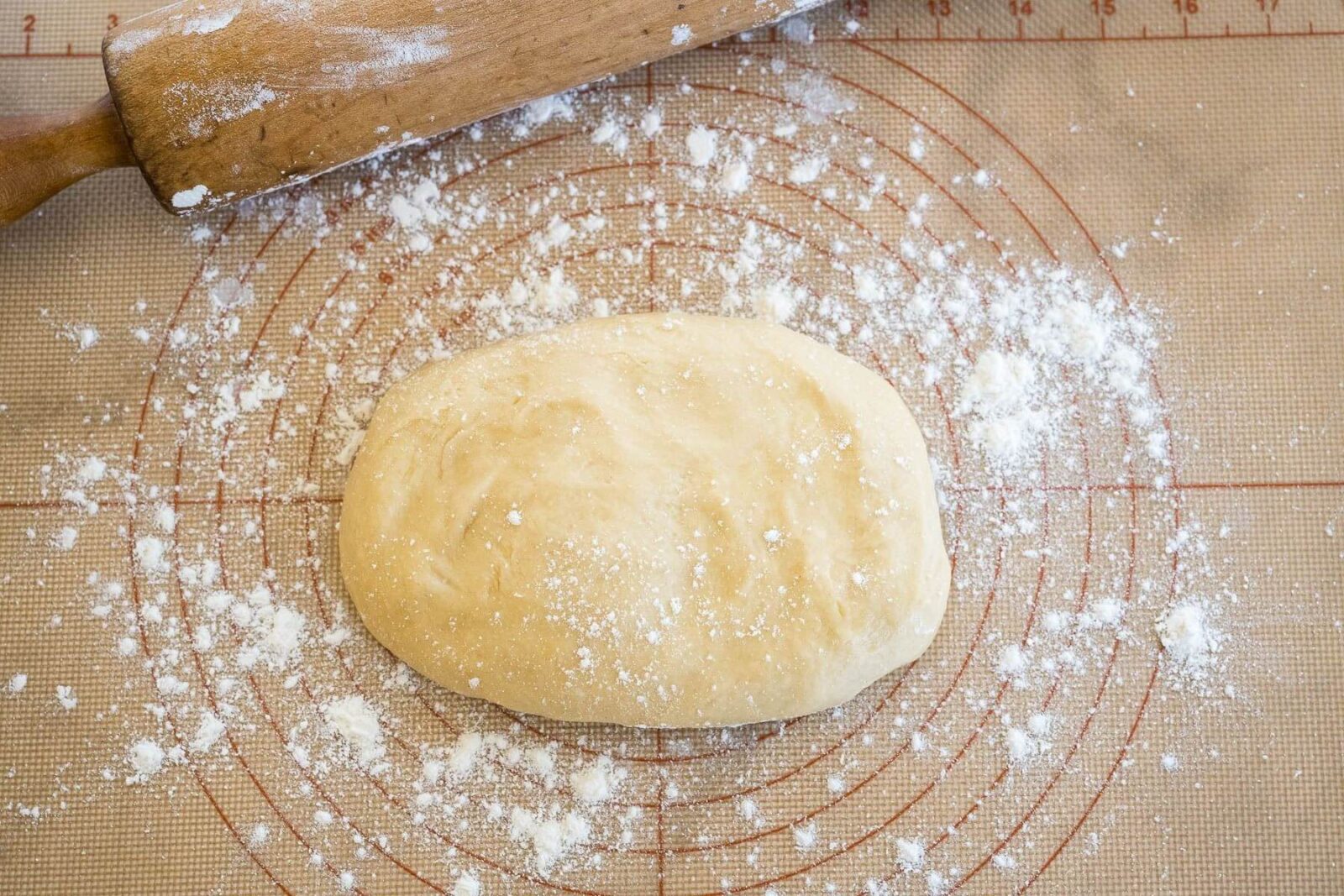 A puffy ball of dough sits on a floured surface next to a wooden rolling pin.