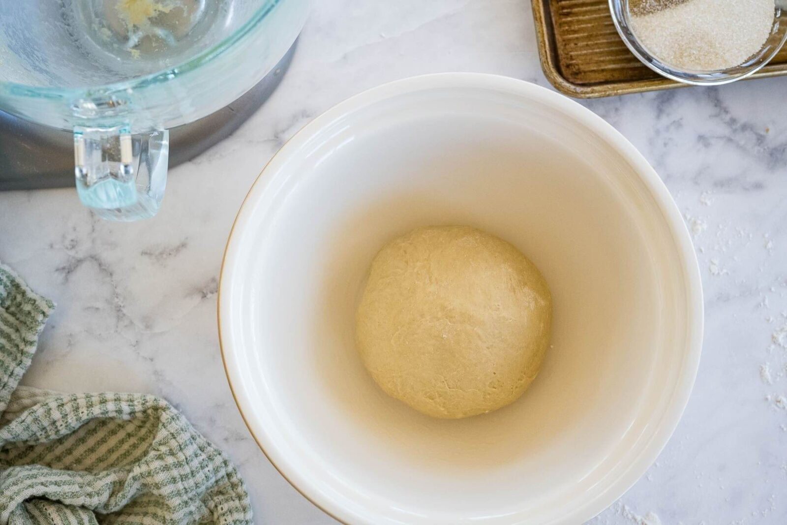 A smooth, puffy dough ball sits and a greased bowl.