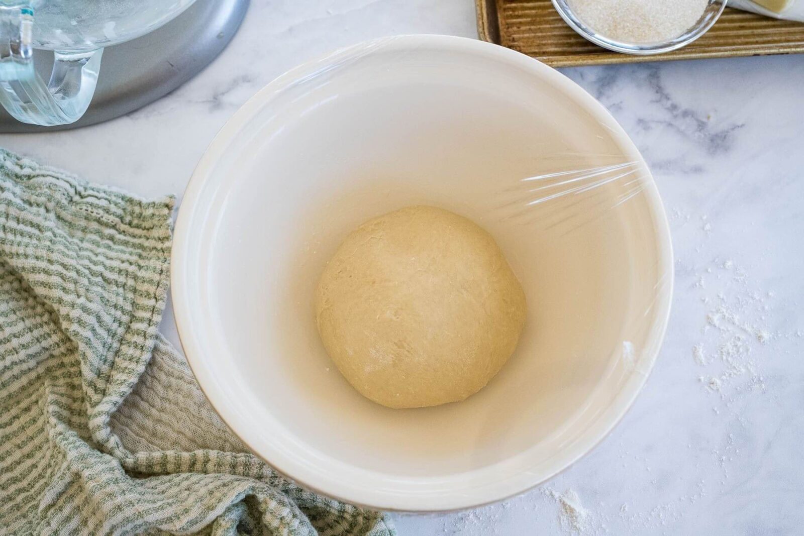 A smooth ball of dough sits in a bowl covered with plastic wrap.