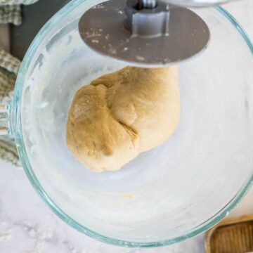 A stand mixer with a kneading attachment has kneaded dough into a solid mass.