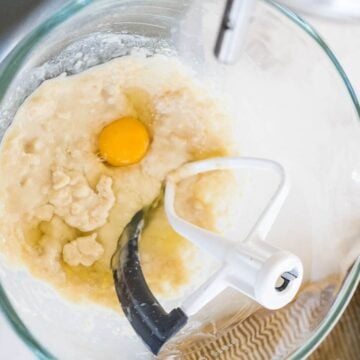 A raw egg sits on a flour dough mixture in a glass bowl.