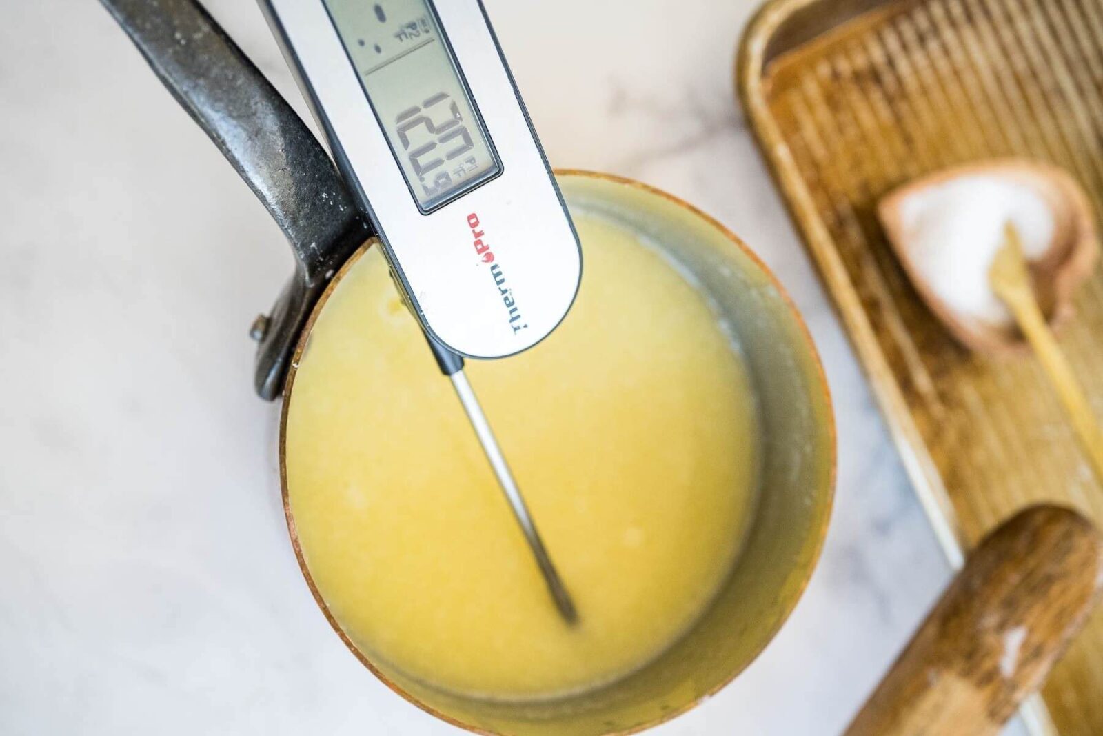A food thermometer measures a melted butter mixture in a saucepan reading 120 degrees.