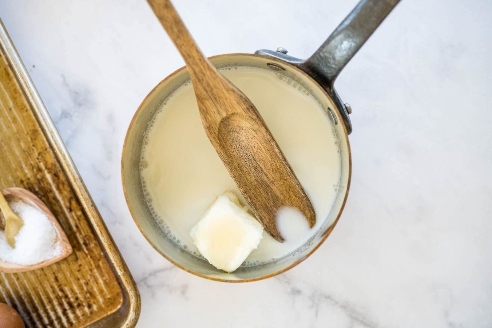 Milk and a chunk of butter sit in a saucepan with a wooden spoon.