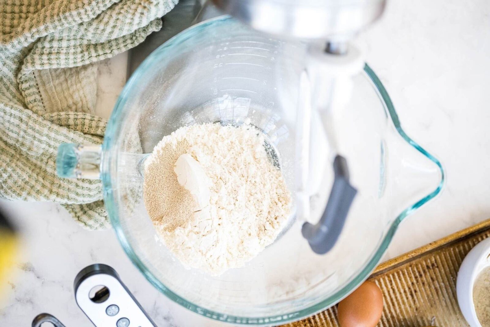 Bread flour sits in a glass mixing bowl with a stand mixer batter attachment above it.