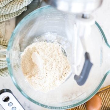 Bread flour sits in a glass mixing bowl with a stand mixer batter attachment above it.