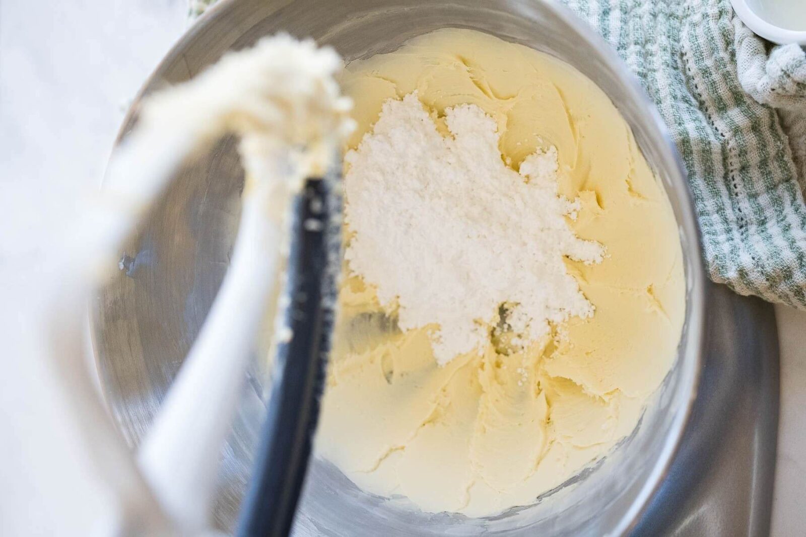 A stand mixer bowl is full of butter mixture and topped with powdered sugar.