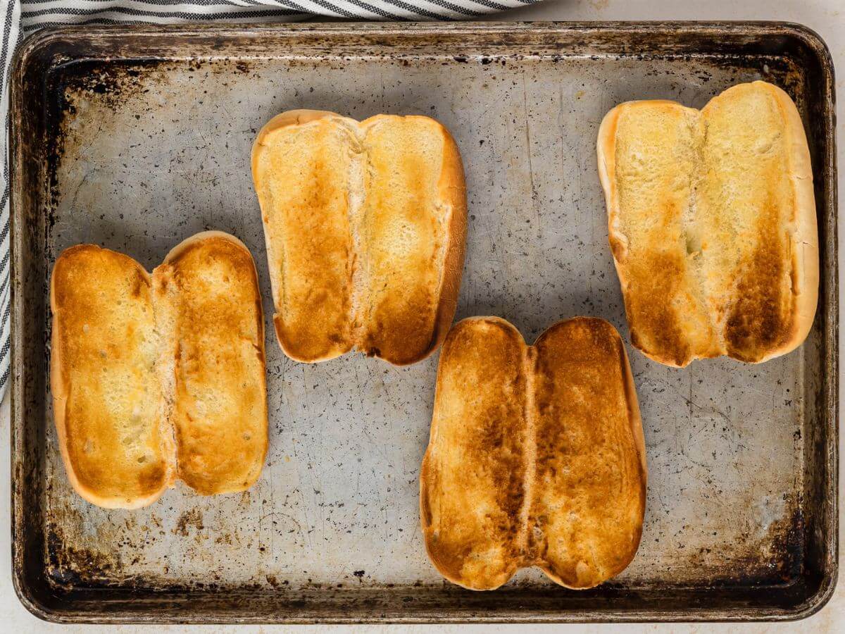 Hoagie rolls buttered and toasted on a sheet pan. 