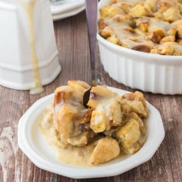 A serving of cinnamon roll bread pudding on a plate, with casserole dish behind and bread pudding sauce.