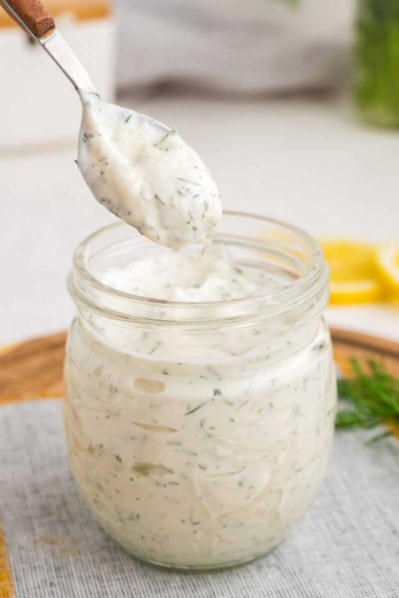 A spoon dips into a jar of white sauce with lemon and dill flavors.