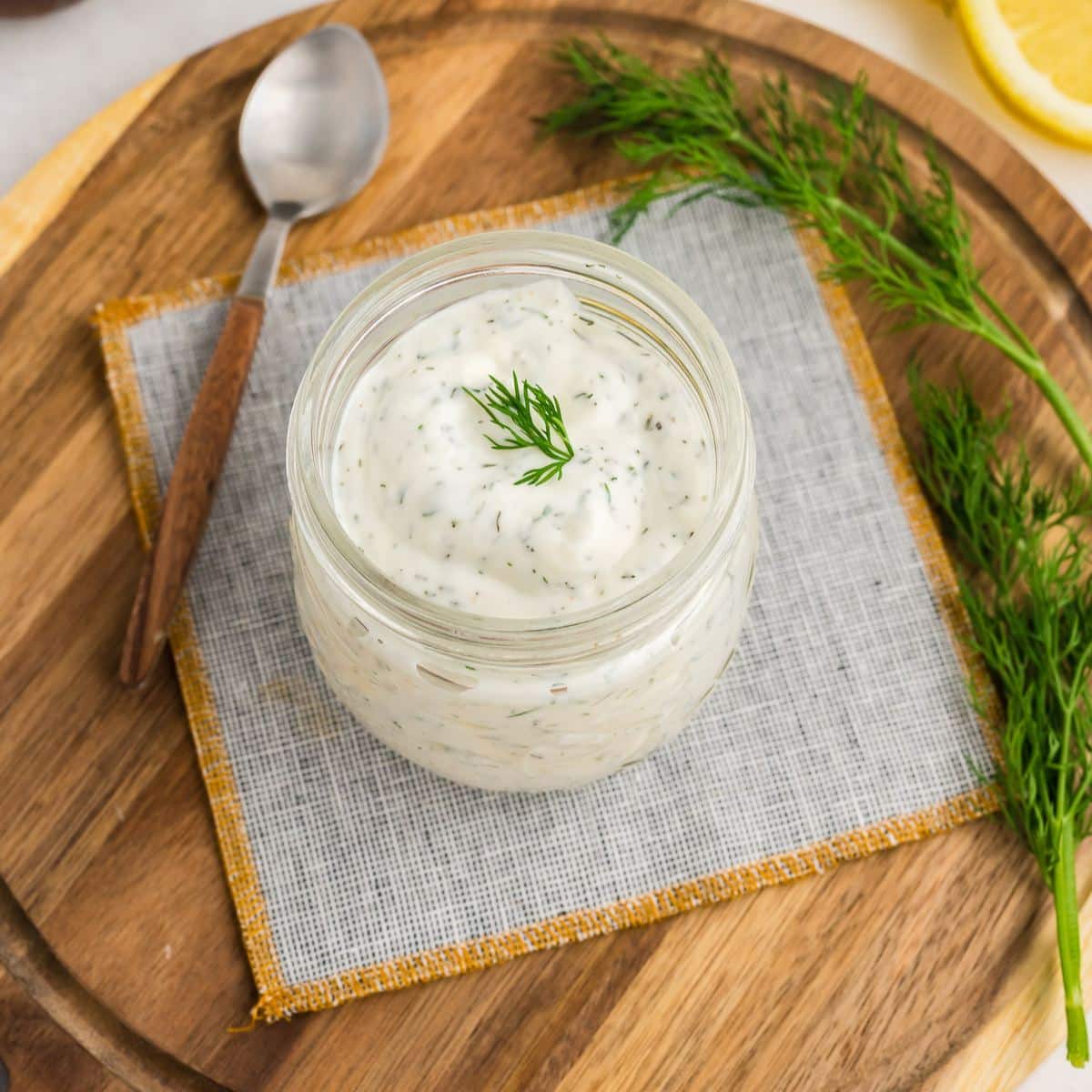 Jar full of creamy lemon dill sauce on a napkin with a spoon.