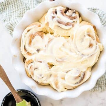 A pie plate filled with 6 cinnamon rolls, frosted.